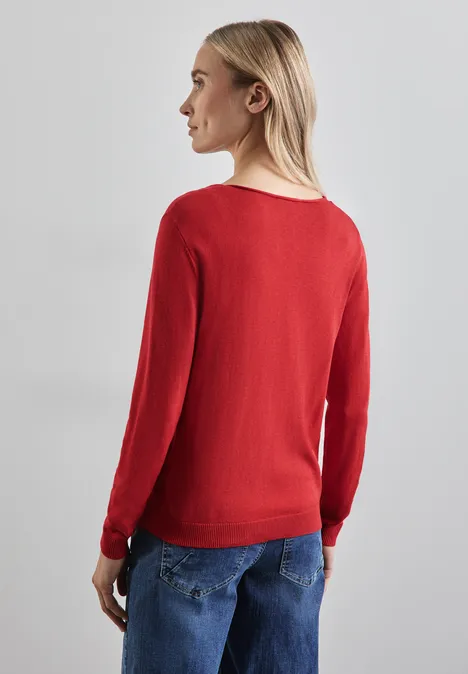 Frau mit langem Haar, rotem Pullover und blauer Jeans von hinten.